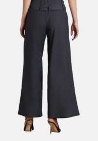 Pantalones de pierna ancha en tejido gris oscuro, con una cintura alta y una textura suave, complementados por un dobladillo limpio y detalles de cinturón.