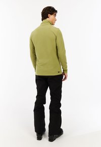 Maglione verde in pile a maniche lunghe con colletto alto e design aderente, abbinato a pantaloni cargo neri e stivali neri.