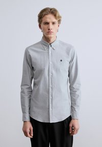 Ανοιχτό γκρι πουκάμισο με κουμπιά από υφή ύφασμα, με μυτερό γιακά, μακριά μανίκια και μικρό κεντημένο λογότυπο στο στήθος.