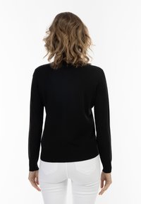 Tricou negru cu mâneci lungi, realizat dintr-un material tricotat moale, cu decolteu rotund și manșete cu nervuri, asortat cu blugi albi.