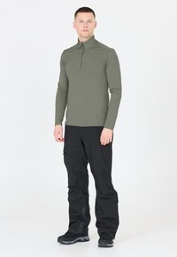 Langærmet, olivengrøn zip-t-shirt parret med sorte, løstsiddende bukser og mørke sko. Glat tekstur, atletisk pasform, minimalistisk design.