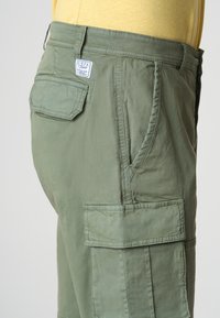 Pantaloni cargo verde oliva realizzati in tessuto leggero, con tasche laterali, una tasca a toppa sul retro e dettagli di cucitura.