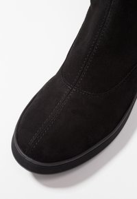 Bottine en daim noir présentant une texture lisse, un bout arrondi, des détails de couture subtils et une semelle en caoutchouc noire avec une prise texturée.