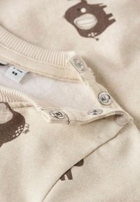 Prenda de bebé de color beige claro con patrones de animales, cuello de canalé y botones a presión para el cierre. Textura suave, tela adecuada para bebés.