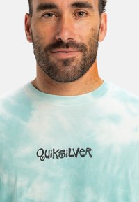 Light blue tie-dye t-shirt made of cotton, with a round neck and the brand "Quiksilver" printed in bold black text on the front.