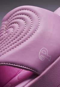 Close-up of a pink slide sandal with quilted heart-shaped stitching and a partial white logo on the strap.