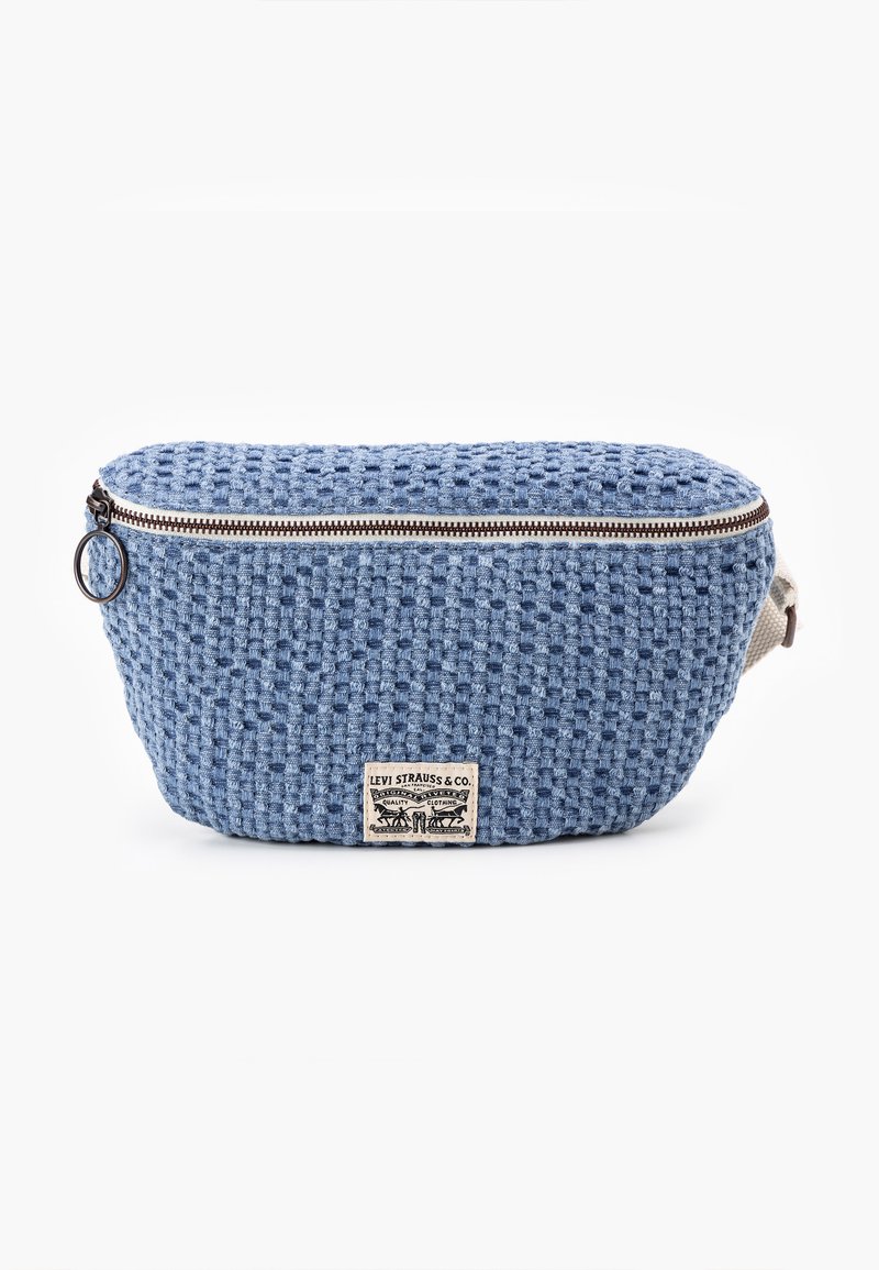 Sac en tissu tissé bleu avec une forme arrondie, doté d'une fermeture éclair, de quincaillerie brune pour la fermeture éclair et d'une étiquette sur le devant.