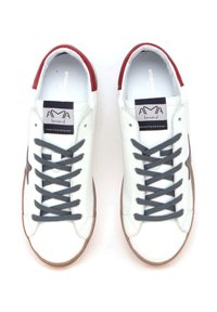 Baskets en cuir blanc avec des lacets gris, accents rouges au niveau du talon et une semelle en caoutchouc marron. Présente le logo de la marque sur la languette.