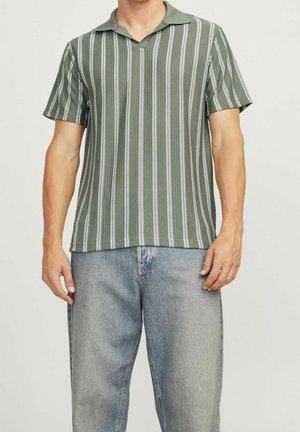 Man wearing green and white vertical striped short-sleeve polo shirt with light blue denim jeans against plain background.