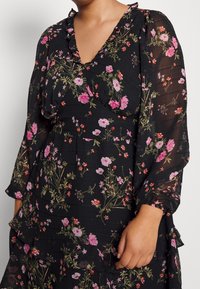 Robes noires à fleurs avec un col à volants et des manches longues. Le tissu est léger avec des motifs floraux roses et rouges.