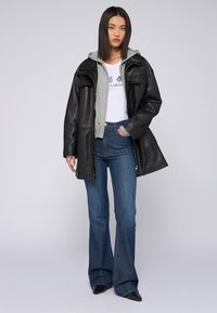 Chaqueta de cuero negra, sudadera gris con capucha, camiseta gráfica blanca, jeans acampanados azules y botas negras de punta. Conjunto urbano simple y en capas.