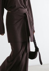 Dark brown knit outfit with a long sleeve top and wrap-around skirt, featuring a matching belt. Soft texture and relaxed fit.
