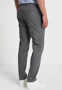Pantaloni grigi su misura in tessuto lavorato, con un design a gamba dritta e tasca posteriore con dettaglio a bottone. Abbinati a sneaker bianche.