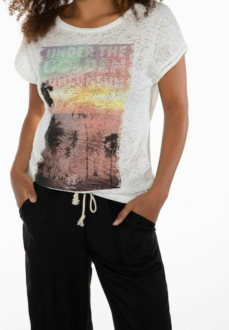 T-shirt blanc à manches courtes avec un imprimé graphique coloré de palmiers et coucher de soleil, texture en superposition, coupe décontractée. Pantalon noir avec cordon de serrage.