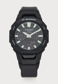Montre G-Shock noire avec un affichage numérique et analogique, marqueurs lumineux, bracelet texturé et plusieurs boutons de fonction sur le côté.