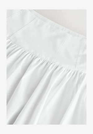 Hvid nederdel med en tætsiddende top og samlet tekstur. Lavet af letvægtsstof, med diskrete sømme og bløde, flydende draperinger.