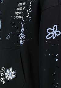 Der schwarze Kapuzenpullover zeigt grafische Designs in Weiß und Hellblau, darunter Blumen, Punkte und handschriftlichen Text. Er verfügt über eine Fronttasche.
