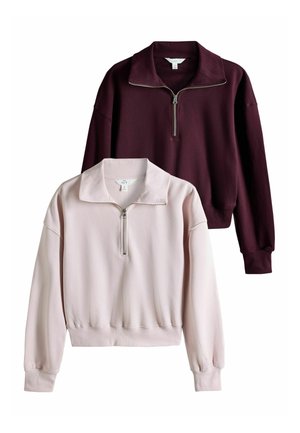 Deux sweat-shirts à manches longues avec demi-fermeture éclair, un rose clair et un bordeaux foncé, affichés sur fond blanc.