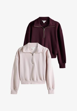 Deux sweat-shirts à manches longues avec demi-fermeture éclair, un rose clair et un bordeaux foncé, affichés sur fond blanc.
