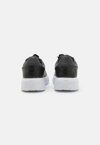 Black leather sports shoes with a white textured sole, featuring a rounded heel and minimal design, visible stitching, and pull tab detail.