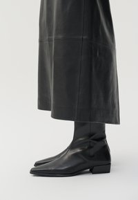Schwarze Leder-Stiefeletten mit spitzem Zehenbereich und niedrigem Blockabsatz. Glatte Textur mit enganliegendem Sitz am Knöchel, keine sichtbaren Beschläge.