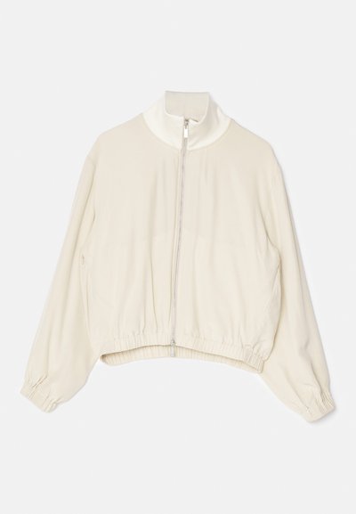 Veste courte beige clair avec un col montant, fermeture éclair sur toute la longueur, poignets élastiques et ourlet froncé ; tissu lisse et doux avec un minimum de détails.