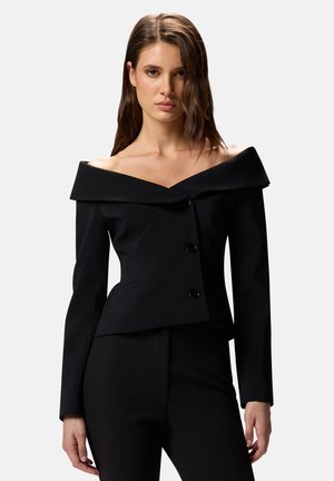 Giacca nera con scollo a barca, colletto strutturato, chiusura frontale con doppio bottone e vestibilità su misura. Il tessuto ha una finitura liscia e texturizzata.