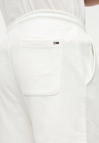 Λευκά βαμβακερά παντελόνια φόρμας με στενή εφαρμογή, ελαστική μέση και πίσω τσέπη με οριζόντια λωρίδα κοντράστ που φέρει λογότυπο.