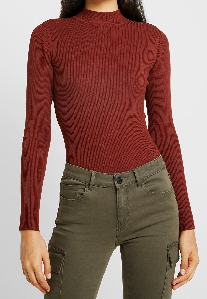 Body de manga larga acanalado en rojo profundo, combinado con pantalones cargo verde oliva que cuentan con bolsillos frontales y cierre de botón.