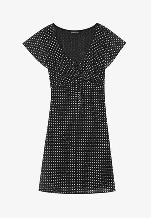 Robe noire à pois blancs, manches courtes, décolleté en V, taille froncée avec un cordon de serrage, et une coupe évasée ample.