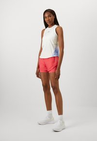 Vitt ärmlöst träningslinne med pastellgradient, kombinerat med rosa shorts. Vita sneakers och strumpor fulländar looken. Enkelt och sportigt design.