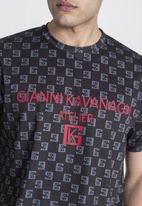 Čierne tričko s krátkymi rukávmi s opakujúcim sa vzorom loga v sivej farbe, s tučným červeným textom "GIANNI KAVANAGH ATELIER" a zvýrazneným logom "K".