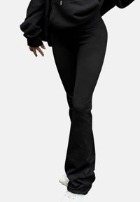 Svarta ribbade utsvängda byxor med en slät textur. Matchade med en svart oversized hoodie och vita sneakers, som visar en avslappnad stil.