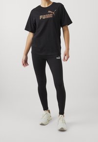 Czarny t-shirt z krótkim rękawem z tygrysim nadrukiem; zestawiony z czarnymi legginsami i jasnymi sneakersami. Gładki materiał, sportowy krój.