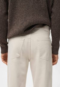 Vaqueros beige de corte recto, tejido texturizado y dos bolsillos traseros. Combinados con un suéter de canalé marrón oscuro.