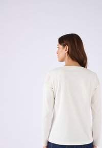 Crème-top met lange mouwen en decoratieve kantaccenten op de schouders, met een gladde textuur en een ronde hals, gecombineerd met donkere jeans.