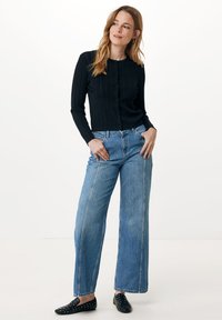 Černý žebrovaný kardigan s dlouhým rukávem a předními knoflíky, kombinovaný s vysokým modro světle širokým džínem a černými slip-on botami se cvočky.