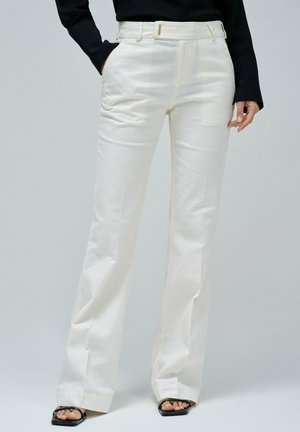 Pantalons larges blancs en tissu lisse, dotés de poches avant et d'une taille ceinturée. Les jambes sont effilées avec une finition soignée.
