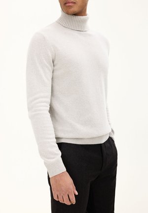 Hellgrauer Rollkragenpullover mit geripptem Kragen und Bündchen, aus weichem Material, kombiniert mit dunklen Hosen.