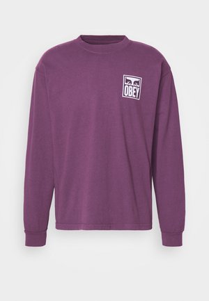 Purple long-sleeve t-shirt made of cotton. Features a white graphic logo that says "OBEY" on the left chest area. Round neckline, relaxed fit.
