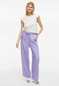 Wit crop-top met gerimpelde mouwen en oogje details, gecombineerd met lichtpaarse wijde broek en witte hakken.