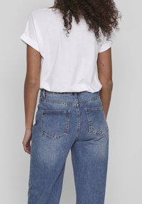 T-shirt blanc à manches courtes associé à un jean en denim bleu taille haute, présentant une coupe décontractée et un design classique de poches arrière.