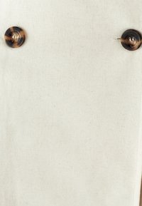 Tessuto di lino beige con una texture liscia, caratterizzato da due grandi bottoni in tartaruga come dettagli notevoli.