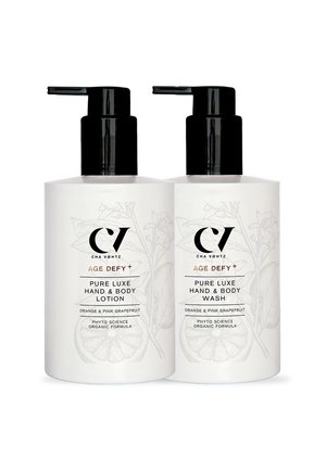 Two white pump bottles labeled "Age Defy+ Pure Luxe Hand & Body Lotion" and "Hand & Body Wash" with orange and pink grapefruit scent.