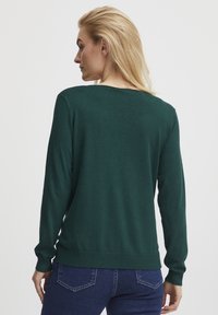 Grüner Pullover aus weichem Stoff, mit langen Ärmeln und rundem Halsausschnitt. Die Rückseite hat eine glatte Textur und einen gerippten Saum.