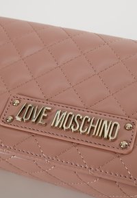 Prošívaná peněženka z růžové umělé kůže s pozlaceným logem "LOVE MOSCHINO" a kovovými hřebíčky s výraznými švy.