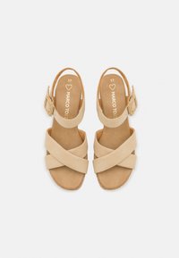 Beige suède sandalen met een kruisband ontwerp, open achterkant en verstelbare enkelband. De binnenzool is bruin en de buitenzool is licht tan.
