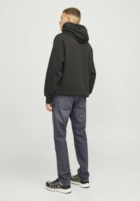 Sweat à capuche noir avec coupe décontractée, assorti à un jean en denim bleu foncé. Les chaussures présentent un détail en mesh noir et gris sur une semelle blanche.