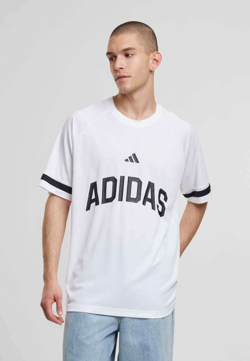 Bela atletska majica s črnim tiskom "ADIDAS", raglan rokavi in črne poudarjene črte na rokavih. Mehka, zračna tkanina.