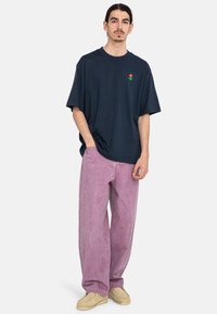 Camiseta de gran tamaño en color navy con un pequeño logo floral multicolor, combinada con pantalones de pana de pierna ancha en color rosa claro y zapatos beige.